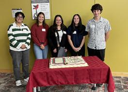 Department first year grad students smiling behind a cake