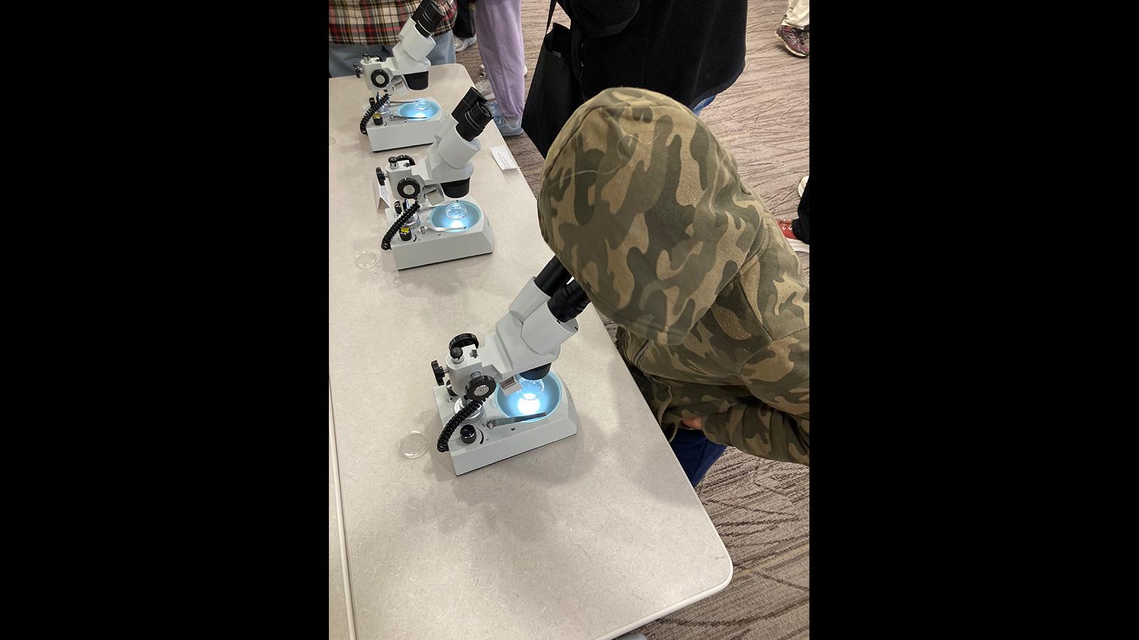 A child in a hoodie looks into a microscope. We think they are excited!