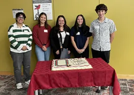 Department first year grad students smiling behind a cake